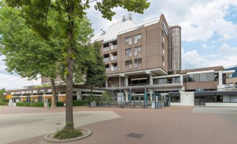 a modern building with a tree in front of it and a bike parked nearby at Leonardo Hotel Lelystad City Center