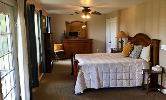 a bedroom with a bed , dresser , and fan is shown in the image , with sunlight streaming through the windows at A Mighty Oak B&B