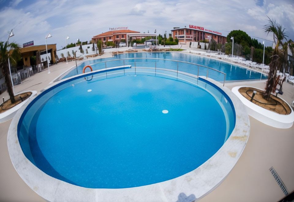 a large , blue swimming pool surrounded by buildings and trees , with people enjoying themselves in the water at Perinthos Hotel