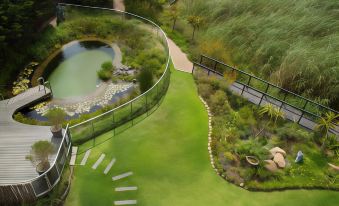 a winding path leads through a lush green garden with a pond and a bridge at Hotel Verde Cape Town Airport