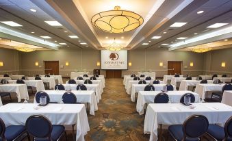 a large conference room with multiple rows of tables and chairs , a projector screen , and a logo on the wall at DoubleTree by Hilton Hotel Murfreesboro