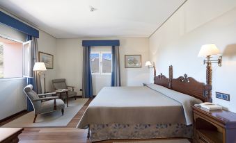 a large bed with a wooden headboard is in a room with a chair , lamps , and framed pictures on the walls at Parador de CAÑADAS Del Teide