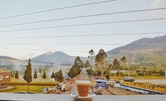 a cup of coffee sits on a table , overlooking a scenic view of mountains and trees at Tani Jiwo Hostel