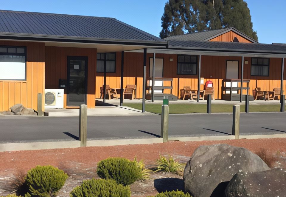 a small wooden house with a sign in front of it , surrounded by trees and grass at Waiouru Welcome Inn