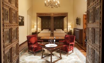 a room with a wooden canopy bed and a wooden table in the center , surrounded by two red chairs at Parador de Leon - San Marcos
