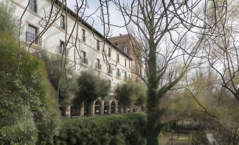 a courtyard with a large building , possibly a hotel , surrounded by trees and bushes , and a path leading to the entrance at Parador de Leon - San Marcos