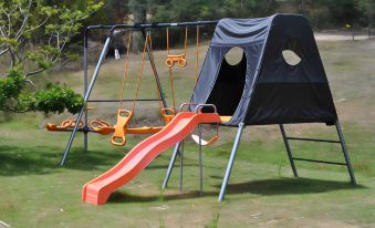 a colorful playground with swings , a slide , and a tent , set in a grassy field at Oyster Cove Chalet