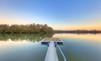 a serene lake scene with a dock extending into the water , reflecting the sky and surrounding trees at sunset at Nambucca River Village by Lincoln Place