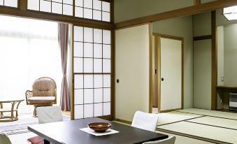 a japanese - style room with a tatami mat floor , a wooden table , and several chairs arranged around it at Ryokan Warabino