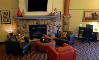 a cozy living room with a fireplace , multiple chairs , and a flat - screen tv mounted on the wall at AmericInn by Wyndham Rogers