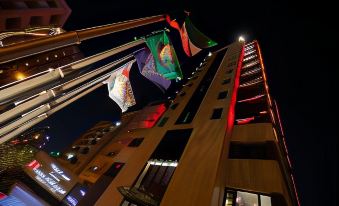 a tall building with multiple flags hanging from it , illuminated at night , creating a festive atmosphere at Swiss-Belboutique Bneid Al Gar Kuwait