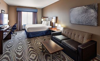 a hotel room with a bed , couch , coffee table , and lamp , all set against a backdrop of a window and patterned carpet at Best Western Plus Williston Hotel  Suites