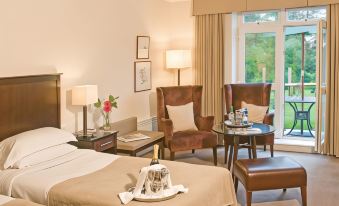 a hotel room with a bed , two chairs , and a table is shown with the curtains open at Macdonald Hill Valley Hotel, Golf and Spa