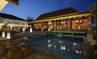 a large pool surrounded by chairs and tables , with a restaurant in the background and lights illuminating the area at Ramada Suites by Wyndham Solo