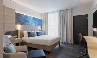 a modern hotel room with a large bed , white curtains , and a black desk in the corner at Courtyard Munich Garching
