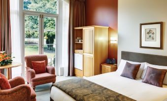 a large bed with a brown and white blanket is in a room with a chair , cabinet , and sliding glass door at Hanmer Springs Hotel