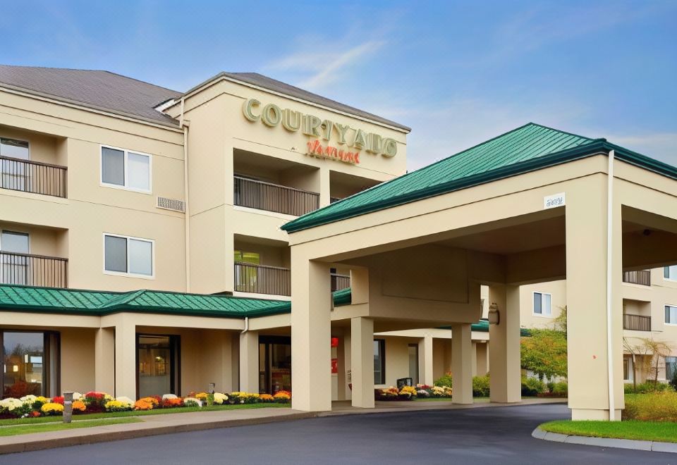 a courtyard by marriott hotel with its entrance and surrounding landscaping , under a clear blue sky at Courtyard Boston Raynham