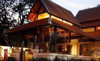 a modern house with a wooden roof and large windows is lit up at night at Parn Dhevi Riverside Resort & Spa