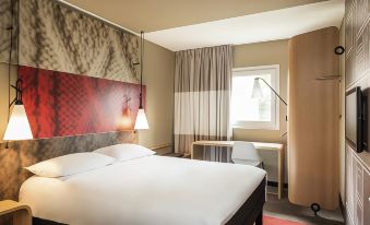 a hotel room with a red and white striped headboard , two lamps on either side of the bed , and a desk in the corner at Ibis Aéroport Bâle-Mulhouse