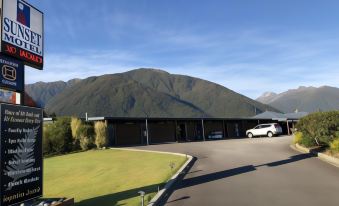 a large building with a car parked in front of it , surrounded by grass and mountains at Sunset Motel