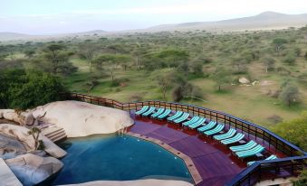 a luxurious outdoor pool area with a unique curved pool , surrounded by trees and mountains , under the sky at Seronera Wildlife Lodge