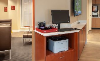a desk with a computer monitor , keyboard , and printer is shown in front of a tv at TownePlace Suites Mobile Saraland