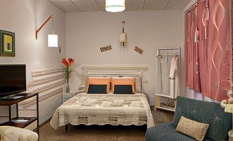 a cozy bedroom with a white bed , pink curtains , and a blue chair in the corner at The Corner Properties