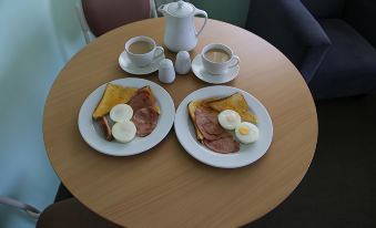 a wooden table with two plates of breakfast food , including eggs and ham , accompanied by cups of coffee at Ballina Colonial Motel