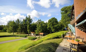 a large grassy field with a house in the background and a tennis court nearby at Fletcher Hotel Restaurant de Wipselberg-Veluwe