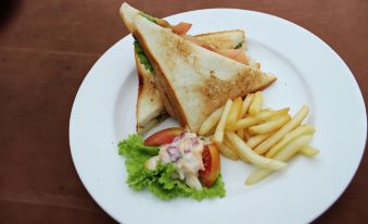 a white plate with a sandwich , fries , and a side salad on a dining table at Surya Yudha Hotel