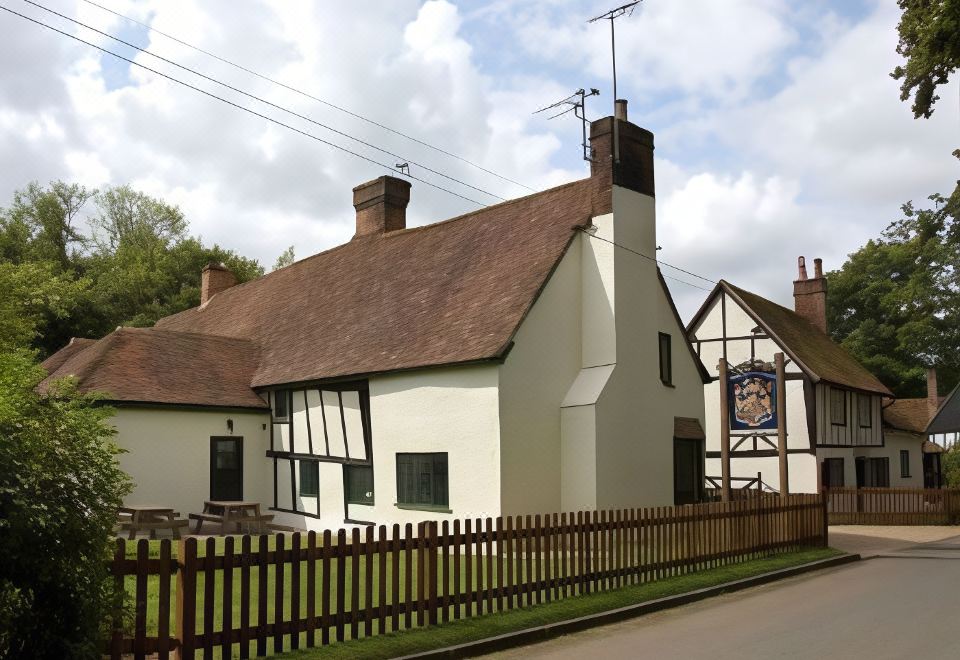 a traditional english village with white and brown cottages , a wooden fence , and a blue sign at The Brocket Arms