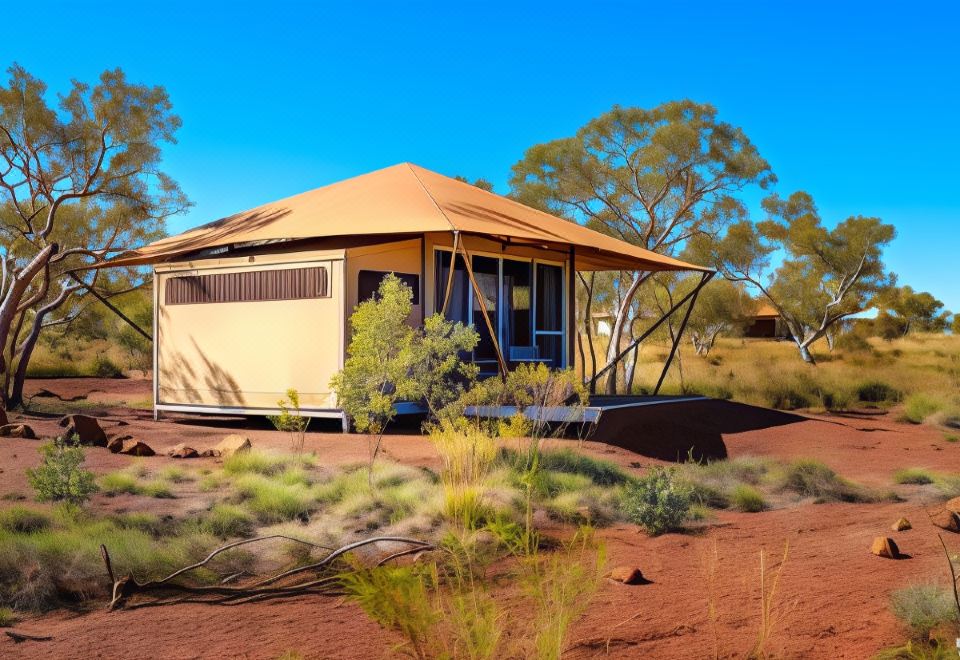 a beige house with a beige roof is surrounded by trees and bushes in a desert setting at Karijini Eco Retreat