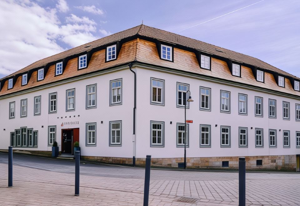 a white building with wooden roof and windows , surrounded by a fence and trees , under a blue sky at Hotel Engel