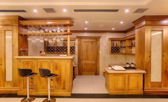 a kitchen with wooden cabinets , wine glasses on the counter , and stools in front of it at Riverside Hotel Quang Binh