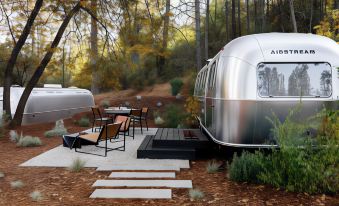 a silver airstream trailer parked on a wooden deck , surrounded by trees and grass at AutoCamp Yosemite