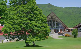 a large green building with a tree in front of it , surrounded by grass and trees at Okushiga Kogen Hotel