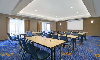 a conference room with blue carpeted floor , wooden tables , and chairs arranged in rows , along with a projector screen on the wall at Courtyard Boston Raynham