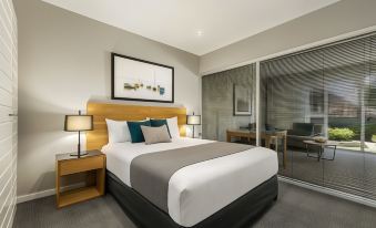 a large bed with a wooden headboard and white linens is in a hotel room at Quest Brighton on the Bay