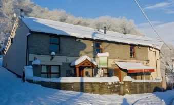 a snow - covered building with a green awning , possibly a pub , surrounded by trees and bushes at The Gwaelod y Garth Inn
