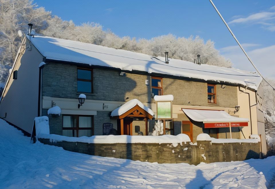 a snowy scene with a building covered in snow and a snow - covered walkway leading up to it at The Gwaelod y Garth Inn