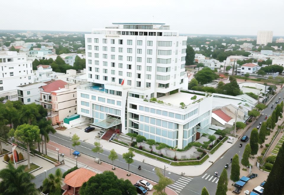 a tall white building with many windows is surrounded by trees and other buildings in an urban setting at Saigon Vinh Long Hotel