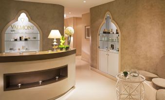 a modern hotel lobby with a curved reception desk and a display case filled with skincare products at Auberge du Jeu de Paume