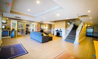 "a spacious lobby with a blue couch , wooden stairs , and american flag , as well as a sign reading "" welcombe ""." at Country Inn & Suites by Radisson, Burlington (Elon), NC