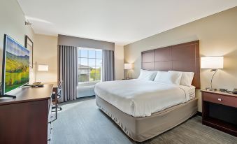 a large bed with white sheets and a brown headboard is in the middle of a room with two lamps , a desk , and a window at Cobblestone Hotel & Suites - Two Rivers