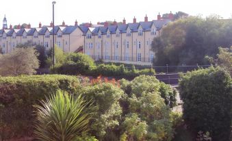 a row of houses with red - tiled roofs is surrounded by greenery and trees , under a clear sky at Maison