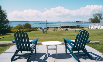 two green adirondack chairs on a deck overlooking a grassy area , with a view of a body of water in the distance at Friars Bay Inn & Cottages