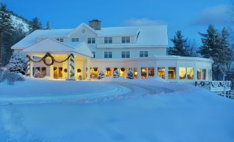 a large white building with a covered porch and christmas decorations , surrounded by snow - covered ground at White Mountain Hotel and Resort