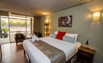 a large bed with a white comforter and red pillows is in a room with wooden floors at The Olive Tree Motel