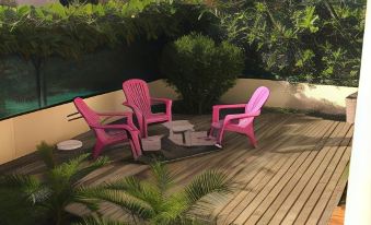 a wooden deck with two pink lawn chairs and a table , surrounded by palm trees and greenery at Marina