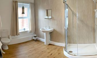 a modern bathroom with a white sink , shower , and wooden flooring , along with a window and two lamps at The Trout Inn